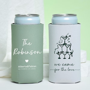 May include: Two can coolers, one sage green and one white, each holding a light blue can. The green cooler has the text "The Robinson", a heart, and the names "Alberta & Fabian" with the date "OCTOBER.25.2026". The white cooler has a martini glass design and the text "we came for the love".