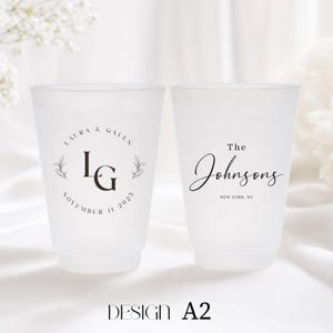 May include: Two frosted plastic cups with custom wedding details. One cup features the initials "LG" with "LAURA & GALEN" and "NOVEMBER 11 2025". The other cup says "The Johnsons" and "NEW YORK, NY". The design is labeled "DESIGN A2".
