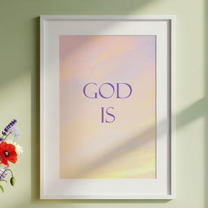 Puede incluir: Un estampado enmarcado con las palabras "GOD IS" en letras moradas sobre un fondo de colores pastel suaves. El estampado está en un marco blanco y cuelga de una pared verde claro. Un jarrón con flores y velas está en un estante debajo.