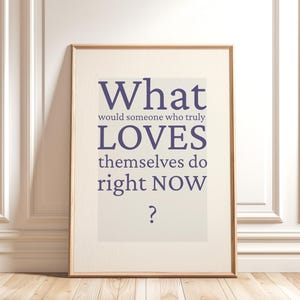 Könnte beinhalten: Gerahmter Druck mit dem Text "What would someone who truly LOVES themselves do right NOW ?" in Dunkelviolett. Der Druck ist in einem hellbeigen Rahmen, der an einer weißen Wand lehnt.