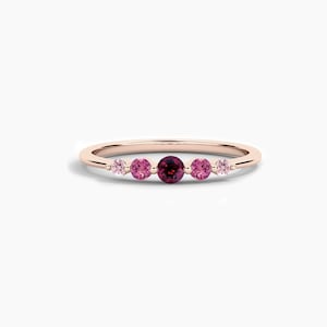 Peut inclure: Une bague en or rose délicate ornée de cinq pierres précieuses. La bague présente une pierre centrale rouge foncé, flanquée de deux pierres roses et de deux pierres roses plus claires. Les pierres sont serties dans un anneau simple et élégant.