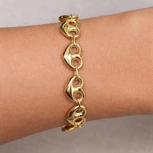 May include: A gold-colored bracelet featuring a series of heart-shaped links. The bracelet is made of a shiny, reflective metal and is worn on a wrist. The design is simple yet elegant, suitable for everyday wear or special occasions.
