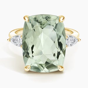 May include: A gold ring with a large, rectangular, light green gemstone. Two pear-shaped, clear gemstones are set either side of the main stone. The ring has a classic design with gold prongs securing the stones.