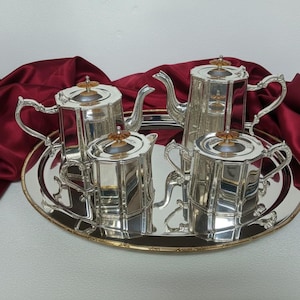 May include: A silver tea service set consisting of a teapot, a coffee pot, a creamer, and a sugar bowl, all featuring octagonal bodies and small amber-colored finials on the lids, arranged on a large, oval, reflective silver serving tray.