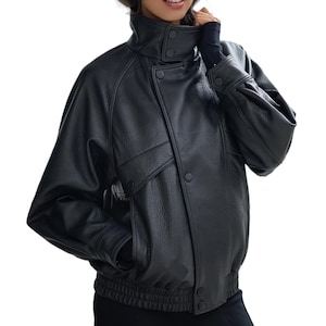Puede incluir: Chaqueta de cuero negra con cuello alto abotonado y dos bolsillos delanteros. La chaqueta tiene dobladillo y puños acanalados. Las mangas son ligeramente sobredimensionadas. Una prenda de abrigo elegante.
