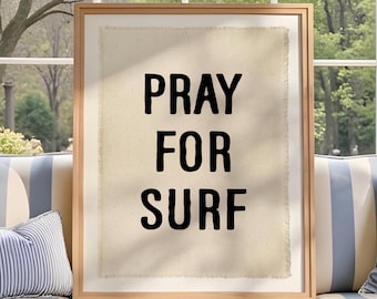 May include: A framed wall art piece featuring a rectangular piece of off-white fabric with frayed edges. The text PRAY FOR SURF is printed in bold, black, sans-serif capital letters centered on the fabric, enclosed in a light wood frame.