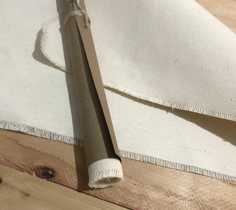 Pode incluir: Uma tela enrolada, embrulhada em papel castanho e amarrada com barbante, repousa sobre uma superf&iacute;cie de madeira ao lado de um grande peda&ccedil;o de tela. A tela tem uma borda crua e desfiada. O rolo de papel est&aacute; parcialmente desenrolado.