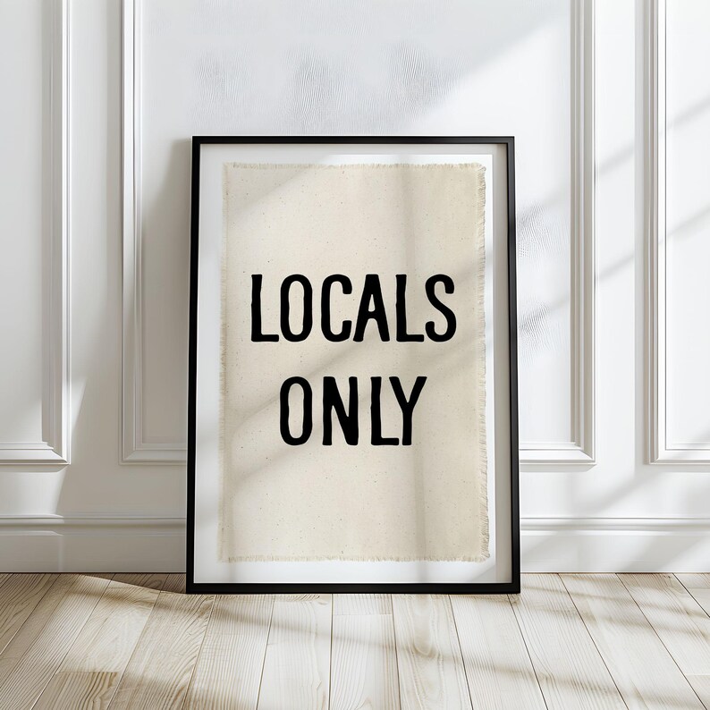 Pode incluir: Uma impress&atilde;o emoldurada com as palavras "LOCALS ONLY" em letras pretas em negrito. A impress&atilde;o tem um fundo texturizado esbranqui&ccedil;ado e est&aacute; emoldurada em uma moldura preta. A obra de arte est&aacute; encostada em uma parede branca em um ch&atilde;o de madeira.