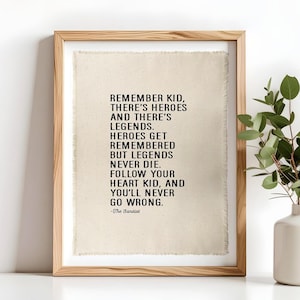 Op de afbeelding: Een ingelijste kunstdruk met zwarte tekst op een lichtbeige stoffen achtergrond met gerafelde randen. De tekst luidt: REMEMBER KID, THERE'S HEROES AND THERE'S LEGENDS. HEROES GET REMEMBERED BUT LEGENDS NEVER DIE. FOLLOW YOUR HEART KID, AND YOU'LL NEVER GO WRONG. -The Sandlot