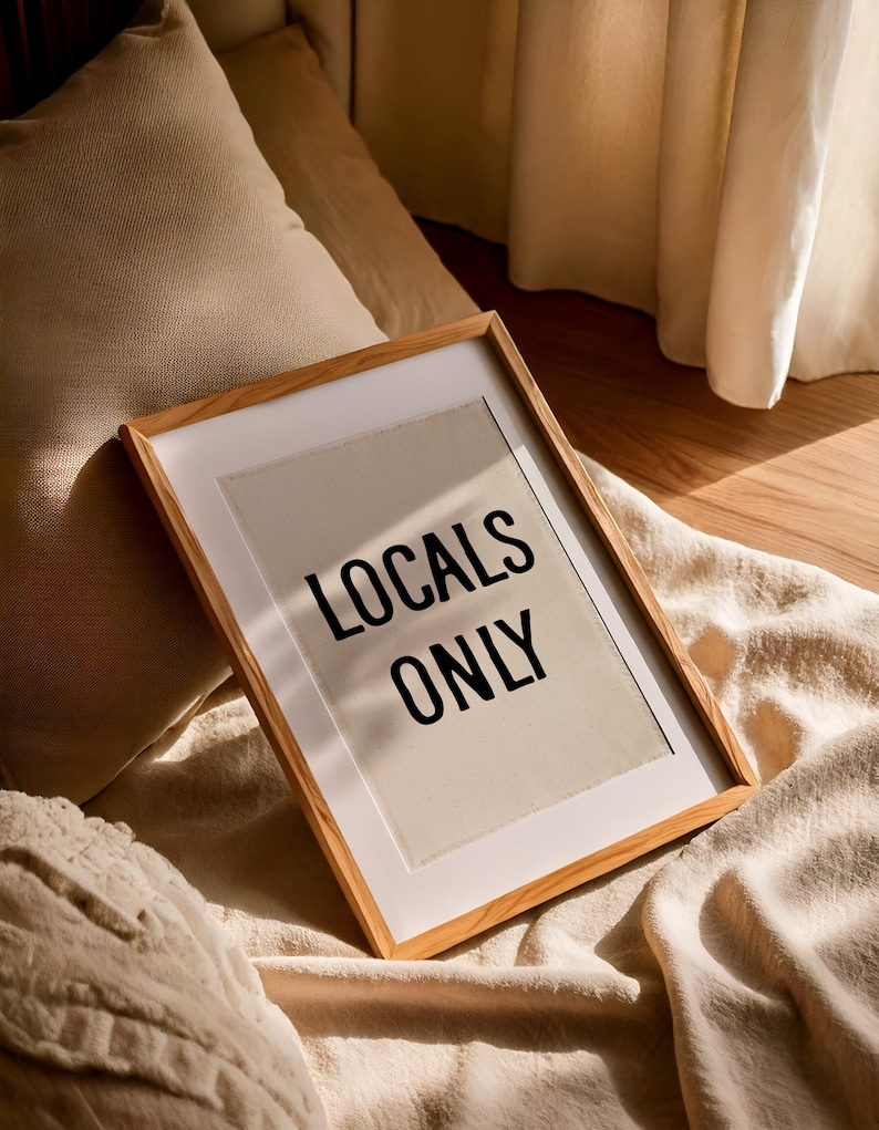 Pode incluir: Uma impress&atilde;o emoldurada com o texto "LOCALS ONLY" em letras pretas. A moldura &eacute; feita de madeira clara, e a impress&atilde;o est&aacute; em um fundo branco. A impress&atilde;o est&aacute; em cima de um cobertor bege.