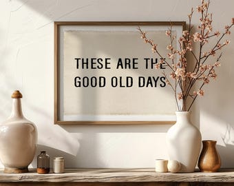 Könnte beinhalten: Ein gerahmter Wandkunstdruck mit dem schwarzen Text "THESE ARE THE GOOD OLD DAYS" auf cremefarbenem Hintergrund. Das Arrangement umfasst eine große beige Vase, eine kleine Glasflasche, eine weiße Vase mit blühenden Zweigen und eine braune Vase.