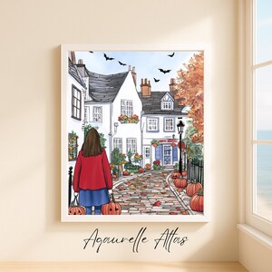 May include: A framed art print depicting a quaint street scene with white buildings, pumpkins, and autumn foliage. A person in a red jacket and blue skirt walks down the cobblestone path, carrying pumpkin-shaped bags. Black bats fly in the sky. The artist's signature is at the bottom.