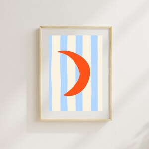 Könnte beinhalten: Ein gerahmter Wandkunstdruck mit einer leuchtend orangefarbenen Mondsichel, die über einem Hintergrund aus vertikalen, handgezeichneten hellblauen und cremefarbenen Streifen zentriert ist. Der Rahmen besteht aus hellem Holz mit einem schlichten Profil.