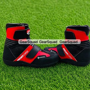 Puede incluir: Un par de botas de moto negras y rojas con el logotipo de Ducati Corse y la marca Gore-Tex. Las botas tienen un diseño de caña alta con correas de velcro ajustables en el empeine y el tobillo, y una suela negra texturizada.