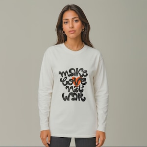 Puede incluir: Camiseta de manga larga color crema con la frase "make love not war" en letras negras y un corazón rojo. La camiseta es de material suave y tiene un corte holgado. Una prenda de declaración.