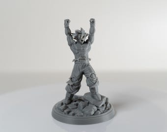 May include: A gray figurine of a muscular male character with spiky hair, arms raised in a triumphant pose. The figure is standing on a rocky base. The figurine is a collectible item.