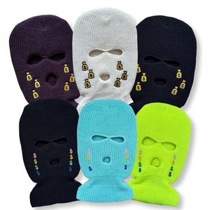 May include: Six knitted balaclavas in various colours: purple, white, navy, black, light blue, and neon green. Each balaclava features embroidered money bag or dollar sign designs around the eye and mouth openings.