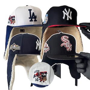 May include: A collection of baseball caps, including a white cap with a blue "LA" logo and a black cap with a white "NY" logo. The caps feature ear flaps and a warm lining, ideal for cold weather. Additional caps include a white cap with a cartoon graphic.