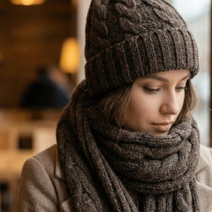 May include: A brown cable-knit beanie and matching scarf set. The hat has a folded brim and a textured, woven design. The scarf is wrapped around the neck and shoulders. The set is made of a soft, warm material, perfect for cold weather.