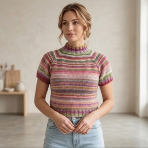 May include: A knitted top with short sleeves and a high neck, featuring horizontal stripes in various colours including pink, green, purple, and brown. The top is paired with light blue jeans. The style is casual and comfortable.