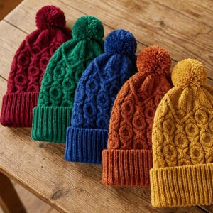 May include: Five knitted beanies with pom-poms in a row on a wooden surface. The hats are in red, green, blue, orange, and yellow. Each beanie has a ribbed brim and a textured, patterned design.