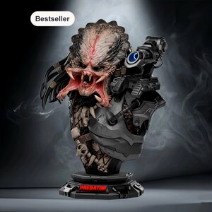 May include: A detailed bust of the Predator alien, featuring a menacing open mouth with sharp teeth and intricate facial details. The sculpture includes a shoulder-mounted weapon and a base with the word "PREDATOR" in red. The bust is a collectible item.