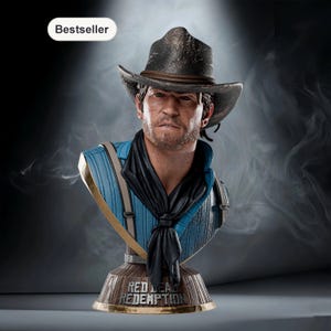 May include: A bust of a man wearing a cowboy hat and a blue shirt with suspenders. The bust has a black scarf tied around the neck. The base of the bust has the words "Red Dead Redemption" in gold lettering.