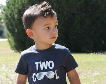 May include: A young boy wearing a navy blue t-shirt with the text "TWO COOL" and a graphic of sunglasses.