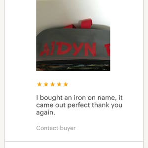 May include: A close-up of a gray backpack with a red iron-on name label that says "AIDYN".