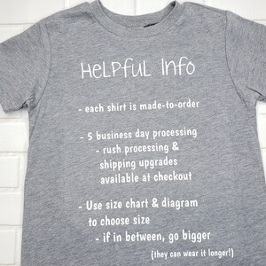 以下が含まれることがあります： 白い文字で「HELPFUL Info」と書かれたグレーのTシャツ。処理時間、配送のアップグレード、サイズに関する情報が含まれています。