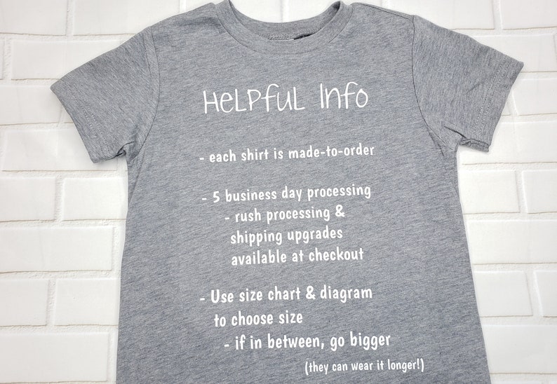 以下が含まれることがあります： 白い文字で「HELPFUL Info」と書かれたグレーのTシャツ。処理時間、配送のアップグレード、サイズに関する情報が含まれています。