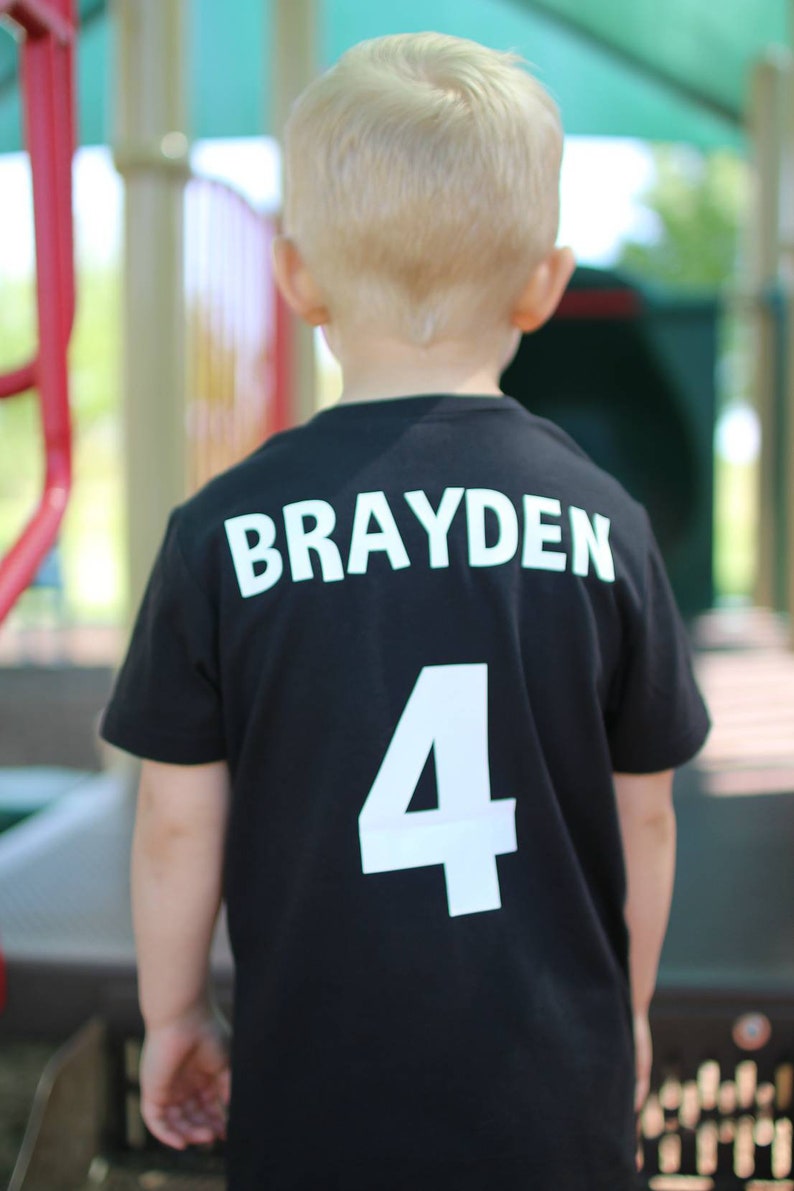 以下が含まれることがあります： 後ろに「Brayden 4」と白文字で書かれた黒いTシャツです。