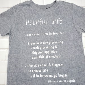 以下が含まれることがあります： グレーのTシャツに、白い文字で「HELPFUL Info」と書いてあり、処理時間、配送のアップグレード、サイズに関する情報が記載されています。