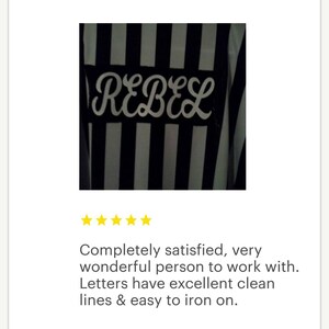May include: A black and white striped iron-on patch with the word "REBEL" in white cursive lettering.