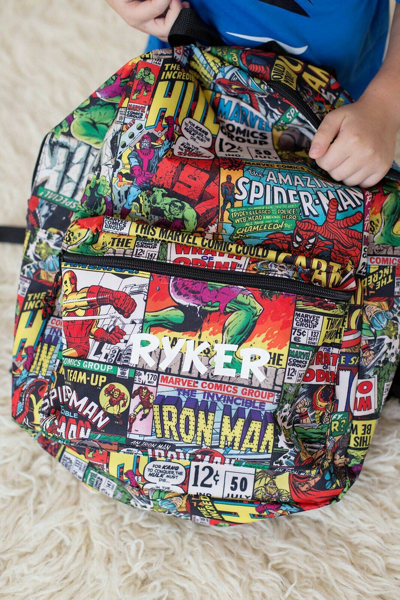 May include: A black backpack with a colorful comic book print featuring Marvel characters like Iron Man, Spider-Man, and the Hulk. The backpack has a white name tag that reads "RYKER".