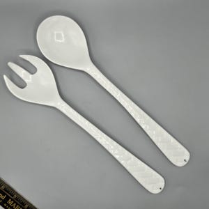 May include: A white ceramic salad serving set with a fork and spoon. The handles of both utensils have a textured design.