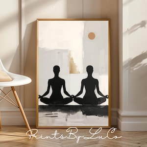Op de afbeelding: Abstracte kunstprint met twee zwarte silhouetten in een yogahouding. Het kunstwerk is geplaatst tegen een neutrale achtergrond met een gouden lijst. De print bevat een zon en de tekst "Prints By LuCo".