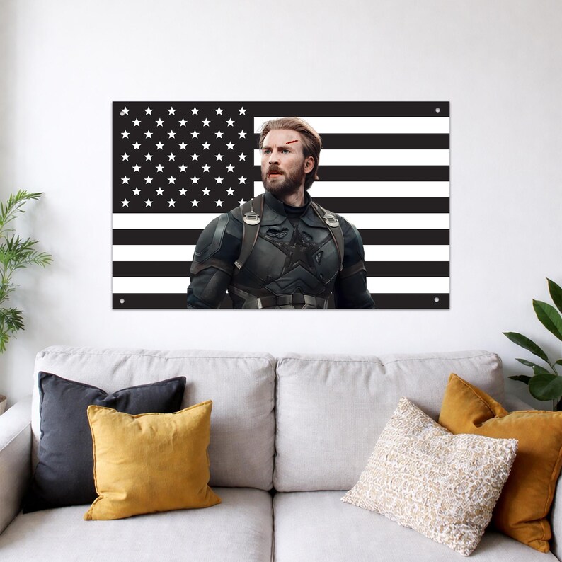 May include: A rectangular wall poster featuring a black and white American flag background with a centered image of a bearded man in a dark tactical suit with a star emblem on the chest and a small red mark on his forehead, mounted with four corner pins.