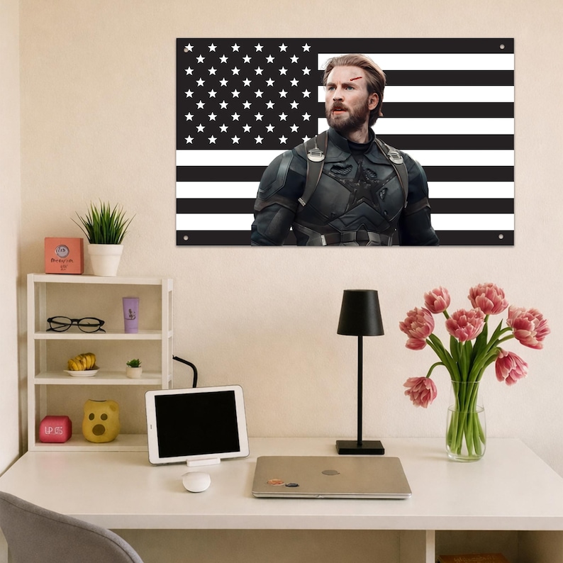 May include: A rectangular wall art print featuring a black and white American flag background with a portrait of a bearded character in a dark tactical suit with a star emblem on the chest, positioned above a desk with a laptop and lamp.