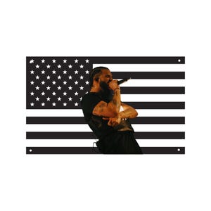 May include: A black and white American flag with a person singing into a microphone. The person is wearing a black shirt and pants. The flag has white stars in the upper left corner and black and white stripes.