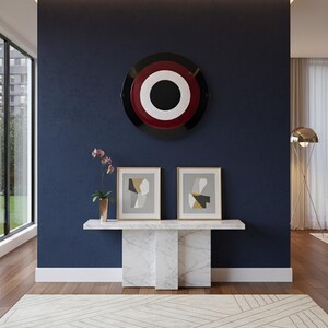 May include: An interior design scene featuring a navy blue wall with a large, circular artwork in black, white, and red. Below, a marble console table displays two framed abstract art pieces. A patterned rug and a gold floor lamp complete the modern aesthetic.