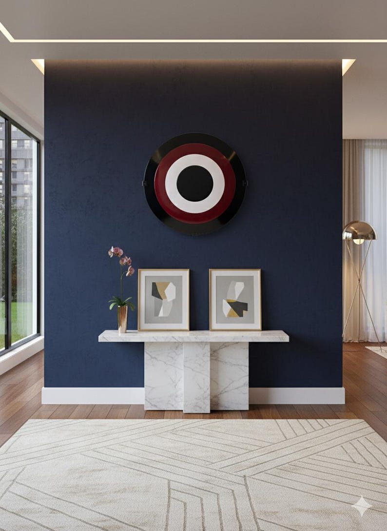 May include: An interior design scene featuring a navy blue wall with a large, circular artwork in black, white, and red. Below, a marble console table displays two framed abstract art pieces. A patterned rug and a gold floor lamp complete the modern aesthetic.