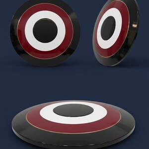 May include: A black, red, white, and gold shield with a circular design. The shield has a black center with a white ring, a red ring, and a gold trim. The shield is shown from multiple angles against a dark blue background.