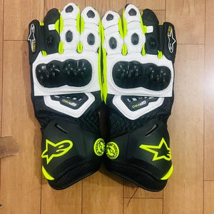 Könnte beinhalten: Paar schwarze und weiße Motorradhandschuhe mit neongelben Akzenten. Die Handschuhe verfügen über eine Schutzpolsterung an Knöcheln und Handflächen, mit dem Text "GP PRO" sichtbar. Die Handschuhe haben ein Sternlogo und andere Markenzeichen.