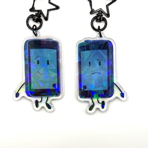 May include: Two clear acrylic keychains featuring cartoon smartphone designs. One has a smiling face, the other a sad face with a cracked screen. Each keychain has a black star-shaped clasp.