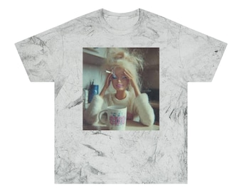以下が含まれることがあります： 白大理石模様のTシャツ。乱れたブロンドの髪のバービー人形がタバコと花のマグカップを持っているプリント画像。人形は白いセーターを着ています。