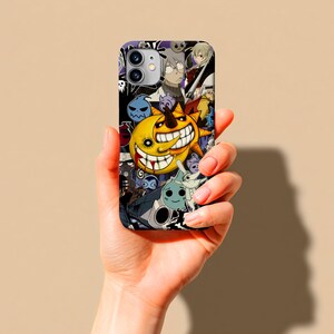 May include: A black and white phone case featuring a collage of anime characters. The case has a yellow sun with a large grin, and other cartoon figures. The phone case is held in a hand.