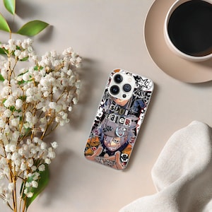 May include: A clear phone case featuring a colorful anime-style graphic with the words "SOUL EATER" in white. The design includes a character with gray hair and a sinister grin. The case is on a light beige surface with a cup of coffee and flowers.