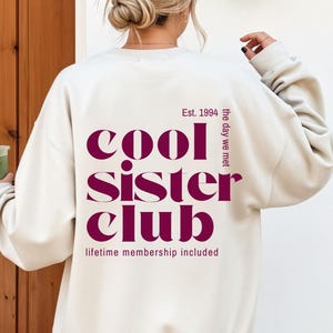 Könnte beinhalten: Cremefarbenes Sweatshirt mit dem Text "cool sister club" in Burgunderrot. Der Text enthält "Est. 1994" und "the day we met". Der Satz "lifetime membership included" ist ebenfalls auf dem Sweatshirt aufgedruckt.