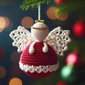 May include: A handmade Christmas ornament in the shape of an angel. The angel is crocheted with a red body, white wings, and a white head with a gold halo. The ornament is hanging from a green Christmas tree branch.
